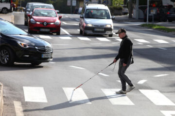 človek z belo palico gre preko ceste po zebri